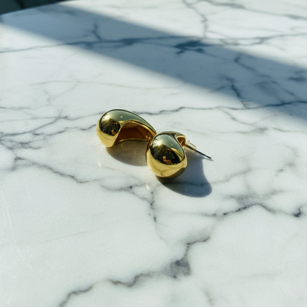 Gold-rimmed sunglasses on a wooden block with a window view in the background Gold Drop Form Earrings stainless steel female womens queens jewellery jewelry Deep Shine Jewellers Your Time To Shine DSJ affordable luxury exclusive craftsmanship