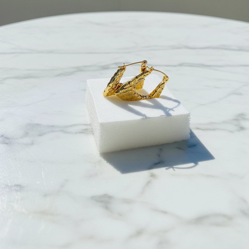 Gold crown on a white stand with a scenic background Gold crown-shaped object on a white stand with a blurred outdoor background gold crocodile design earrings stainless steel exclusive Deep Shine Jewellers DSJ jewellery jewelry Your Time To Shine queens womens ladies kingdom