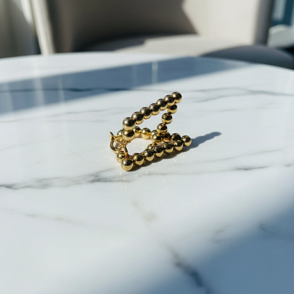 Gold necklace on a white box with a window and buildings in the background Gold beaded earrings on a blue surface stainless steel gold exclusive earrings Deep Shine Jewellers DSJ jewellery jewelry queens ladies womens kingdom Your Time To Shine