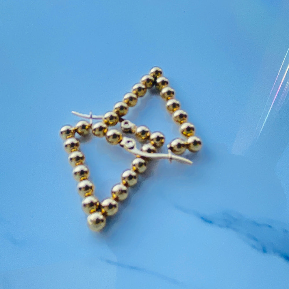 Gold beaded earrings on a blue surface stainless steel gold exclusive earrings Deep Shine Jewellers DSJ jewellery jewelry queens ladies womens kingdom Your Time To Shine