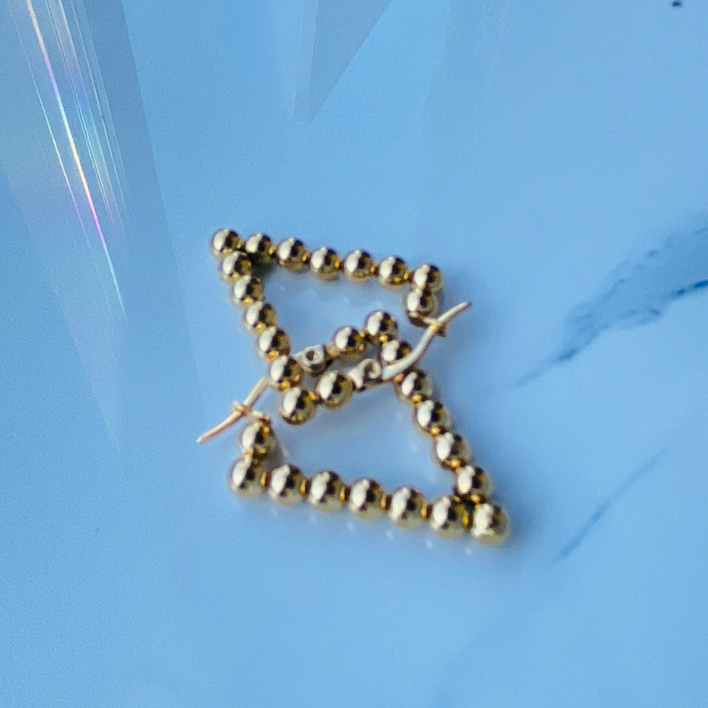 Gold triangle-shaped earrings on a light blue background Gold beaded earrings on a blue surface stainless steel gold exclusive earrings Deep Shine Jewellers DSJ jewellery jewelry queens ladies womens kingdom Your Time To Shine