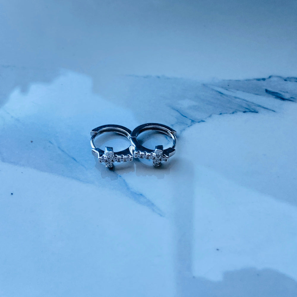 Pair of silver earrings on a white marble surface white gold/silver crossed ice earrings cubic zirconia diamonds sleeper hoop Deep Shine Jewellers Jewellers jewelry DSJ. exclusive affordable jewellery Your Time To Shine 925 silver sterling silver 