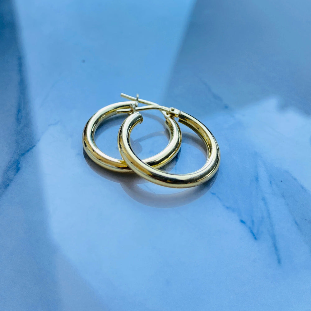 Gold hoop earrings on a reflective blue surface Gold silver sleepers for mens women kings queens man lady kingdom exclusive by Deep Shine Jewellers jewellery jewelry affordable luxury shinning DSJ Your Time To Shine Cape town craftsmanship 