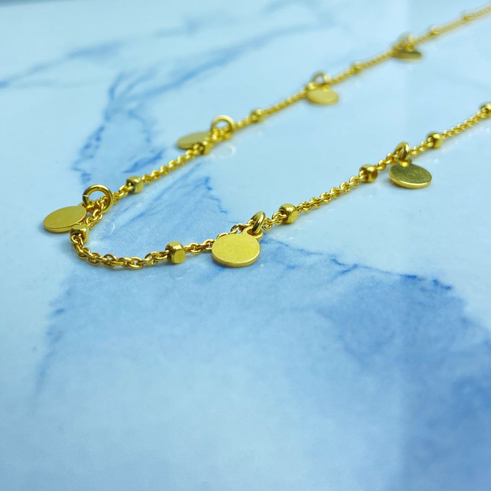 Gold necklace with heart and round pendants on a marble surface