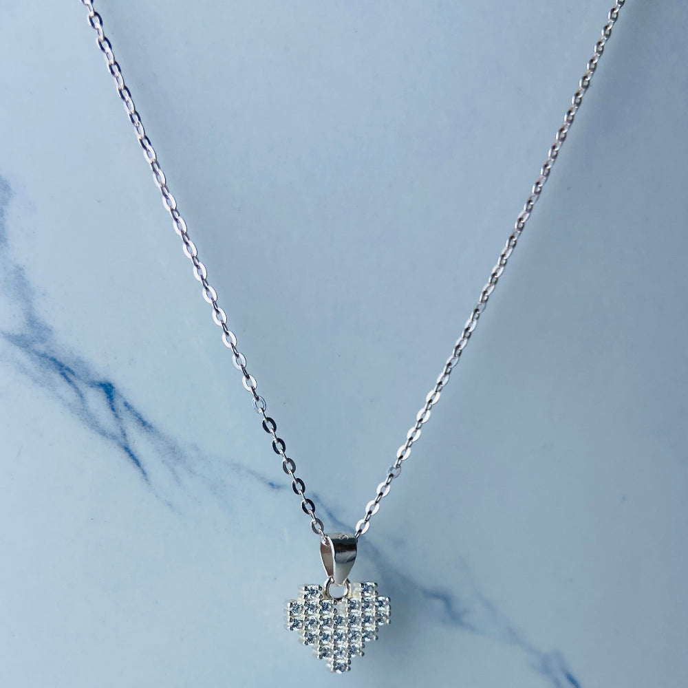 Silver necklace with a heart-shaped pendant on a light blue marble background Silver butterfly-shaped earrings on a marble surface Radiant Silver Pixelated Heart Necklace and Earrings Set by Deep Shine Jewellery women ladies queens 925 silver sterling silver cubic zirconia gemstone diamond lab diamond exclusive craftsmanship cape town artisans affordable luxury best seller trending christmas sale gift wishlish Your Time To Shine DSJ online store shop now 