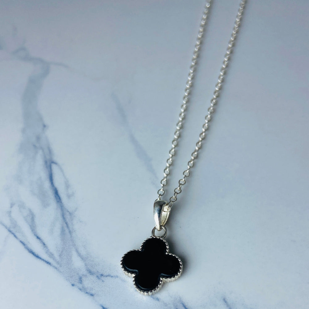 Necklace with a black clover pendant on a marble surface Silver necklace with a floral pendant on a marble surface white gold silver onyx clover pendant necklace chain exclusive craftsmanship affordable luxury premium jewellery jewelry ladies women queens Deep Shine Jewellers DSJ Your Time To Shine best seller trending 925 silver sterling silver Van Cleef and Arpels lucky clover gemstone VC&A