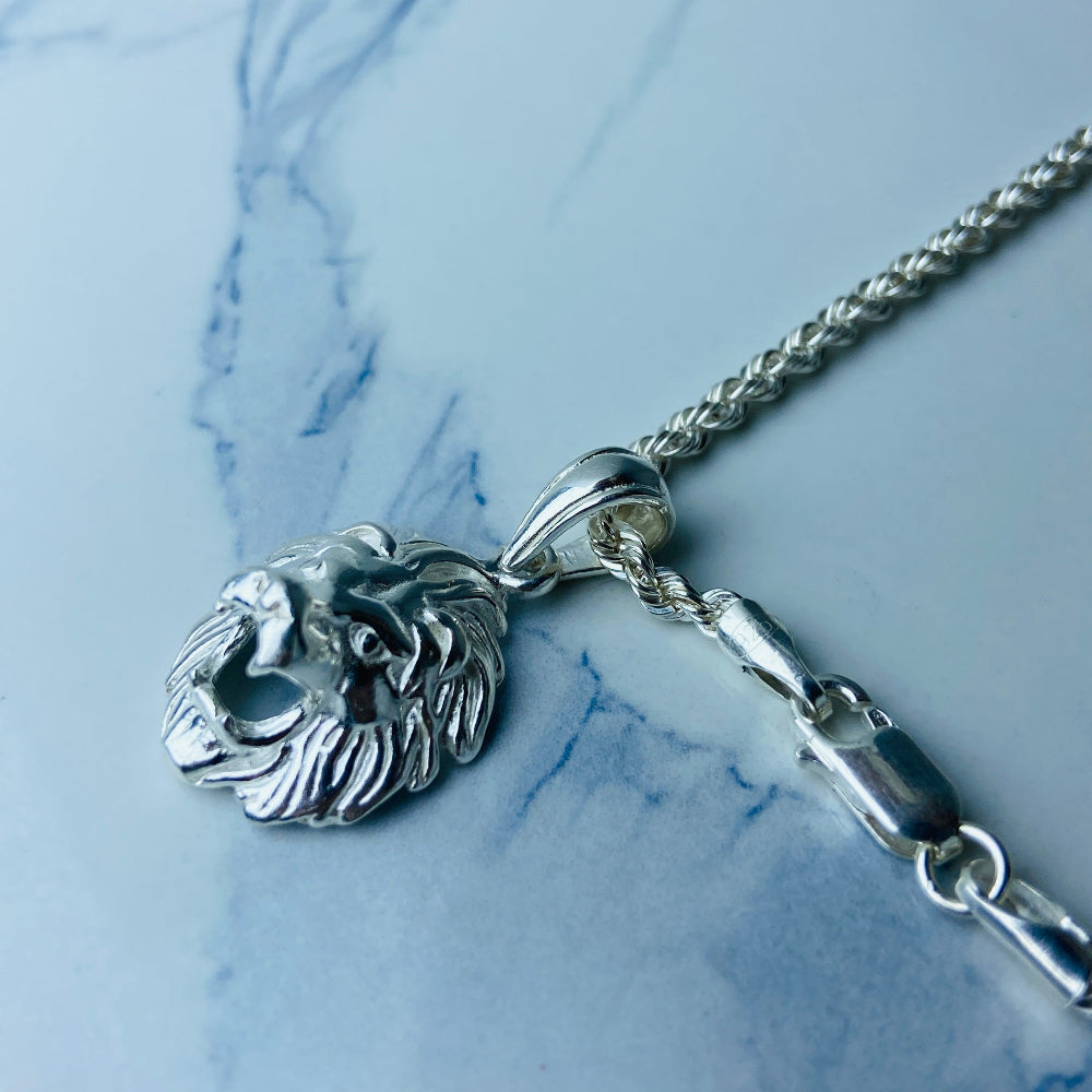 Silver necklace with a lion head pendant on a marble surface Silver lion head pendant on a chain against a marble background Silver Lions head pendant necklace marble surface pendant necklace curb chain exclusive craftsmanship affordable luxury premium jewellery jewelry ladies women queens kings mens gents Deep Shine Jewellers DSJ Your Time To Shine best seller trending 925 silver sterling silver cape town artisans christmas gifts present festive season holiday gifts for love ones