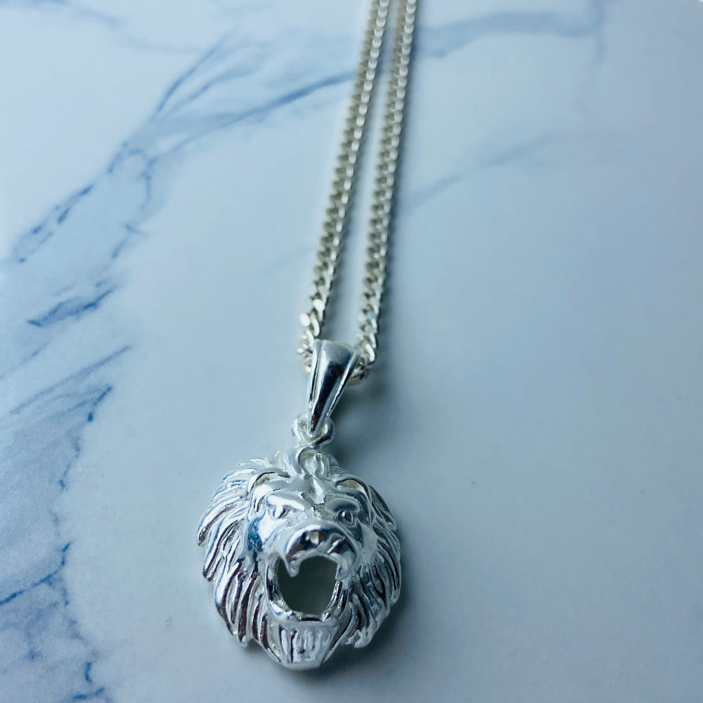Silver necklace with a detailed pendant on a marble surface Silver lion head pendant on a chain against a marble background Silver Lions head pendant necklace marble surface pendant necklace curb chain exclusive craftsmanship affordable luxury premium jewellery jewelry ladies women queens kings mens gents Deep Shine Jewellers DSJ Your Time To Shine best seller trending 925 silver sterling silver cape town artisans christmas gifts present festive season holiday gifts for love ones