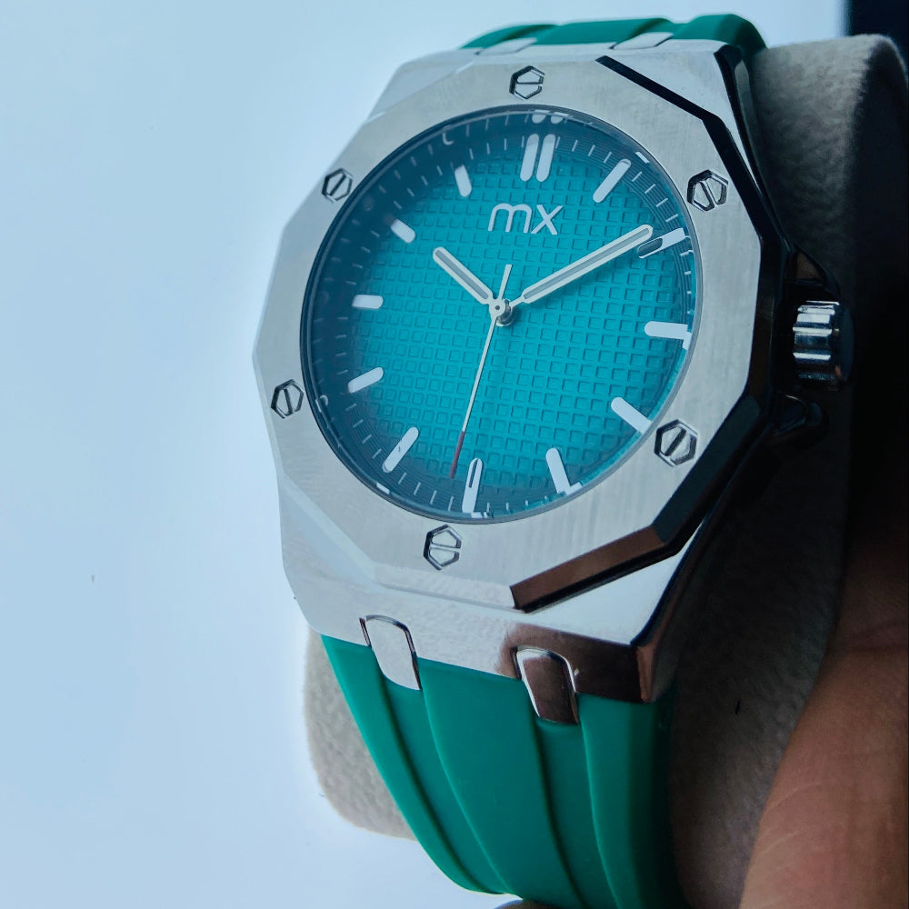 Turquoise watch with silver accents held against a light blue background Wristwatch with green strap and blue face on a white background silver watch with black and blue face on a white marble surface MX mens watch stainless steel watches timepiece timeless luxury best seller trending Deep Shine Jewellers DSJ Your Time To Shine quartz movement black dial gold stick markers 36mm gold bezel rubber strap green christmas sale xmas present holiday season festive season 