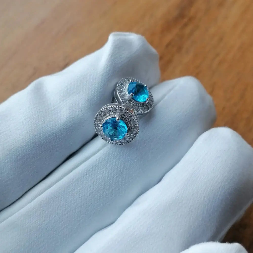 White gold silver earrings featuring vibrant blue gemstone and clear accent stones