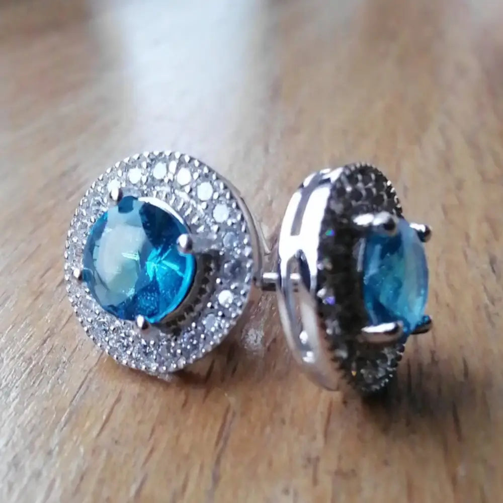 Silver-toned stud earrings with blue gemstones and clear halo in Aqua Radiance White Gold Silver style