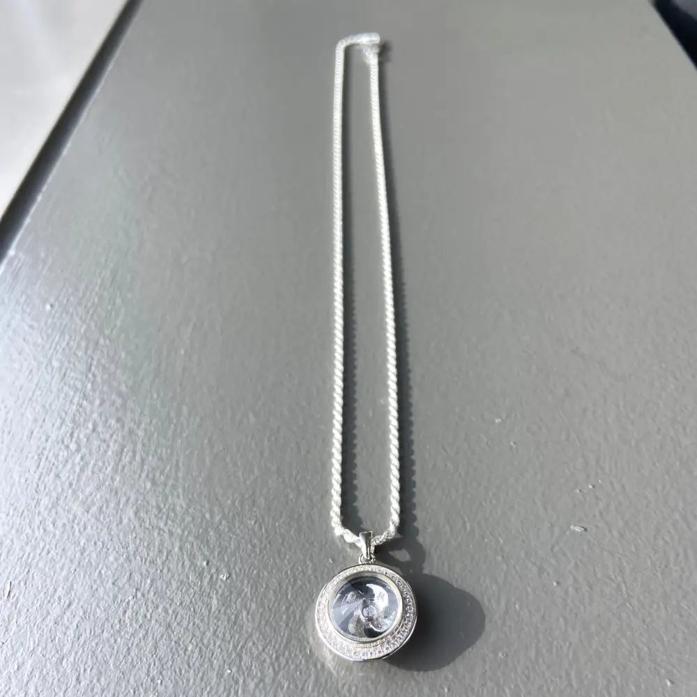 Silver flooded spinning chain necklace with a round clear locket pendant featuring a swirling design