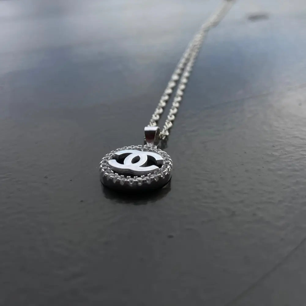 Silver Chanel necklace with circular encrusted pendant featuring interlocking C’s for timeless elegance